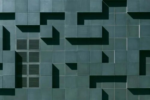 Abstrakte Gebäudefassade mit dunkelgrünen, geometrisch versetzten Paneelen.